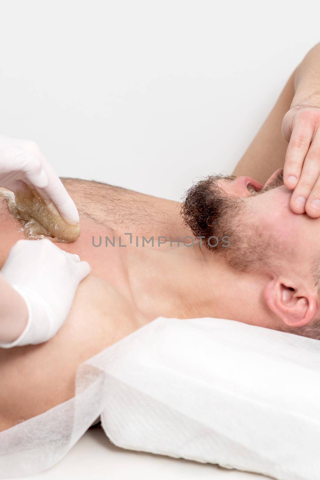 Epilation chest of young male with liquid wax paste by hands of female cosmetologist in beauty salon