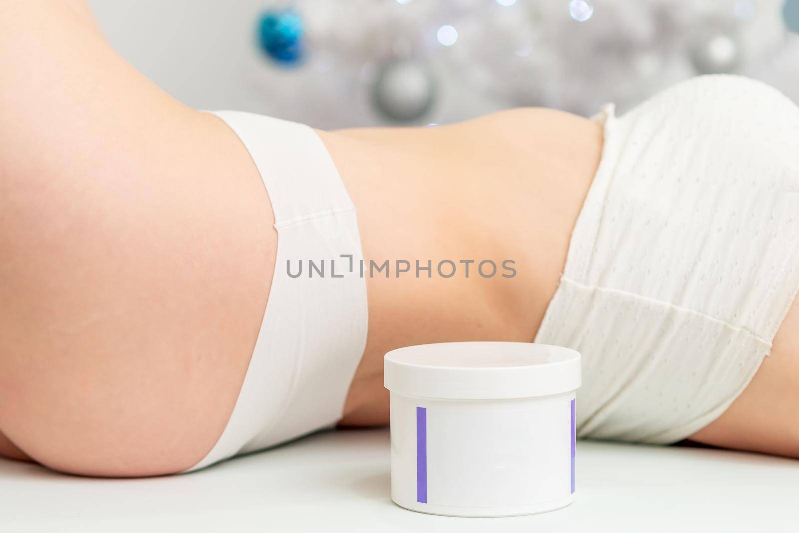 Cosmetics white jar near lying woman body on christmass tree background. Concept of New Year discounts