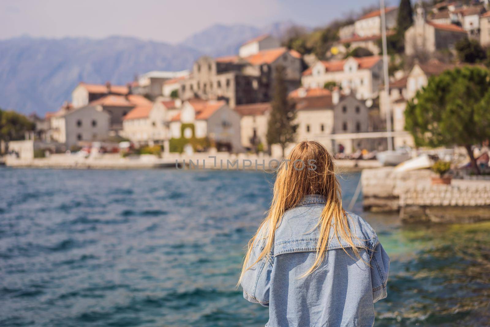 Woman tourist enjoying Colorful street in Old town of Perast on a sunny day, Montenegro. Travel to Montenegro concept. Scenic panorama view of the historic town of Perast at famous Bay of Kotor on a beautiful sunny day with blue sky and clouds in summer, Montenegro, southern Europe by galitskaya