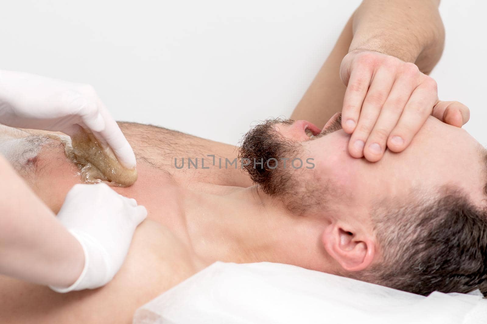 Epilation chest of young male with liquid wax paste by hands of female cosmetologist in beauty salon