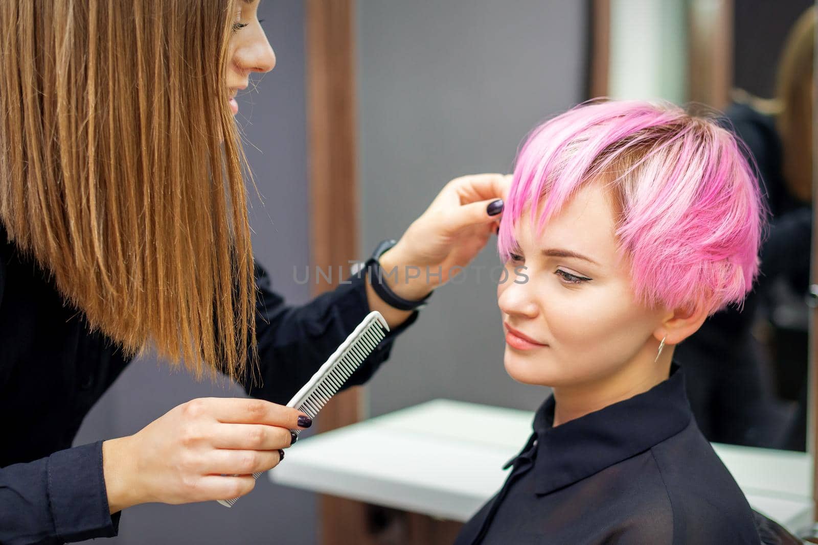 Young woman receiving short pink hairstyle by female hairdresser in beauty salon