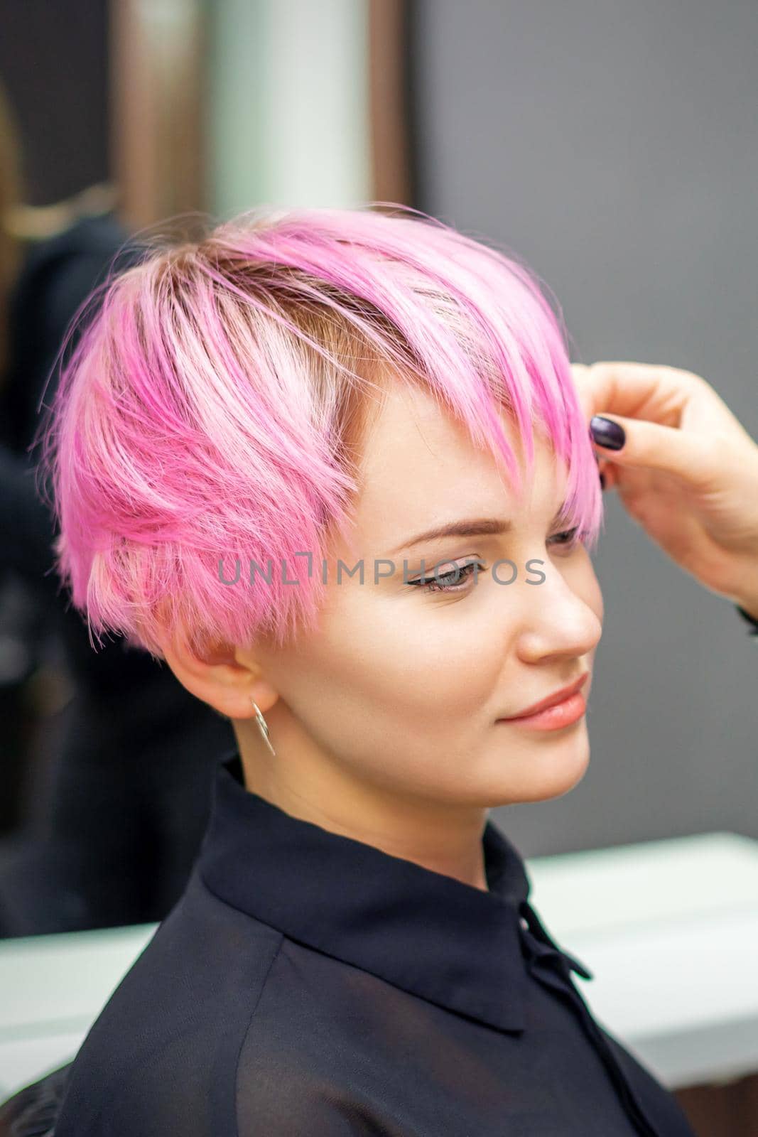 Young woman receiving short pink hairstyle by female hairdresser in beauty salon