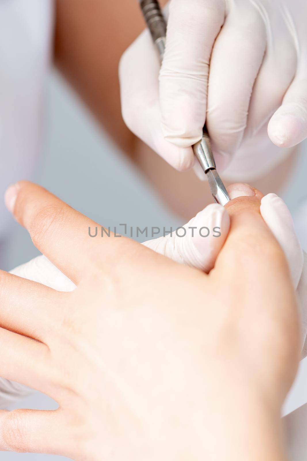 Hands of manicurist pushing cuticles on female's nails with manicure tool. Woman receiving manicure and nail care procedure