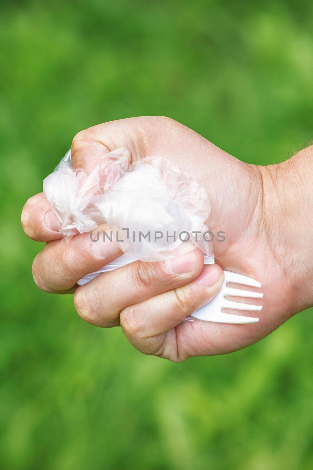 Hand of a man holding plastic trash on a background of green grass in the park