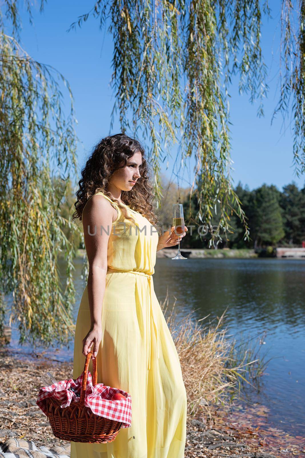 Leisure, free time. Beautiful caucasian woman in yellow dress on a picnic outdoors, sitting next to water