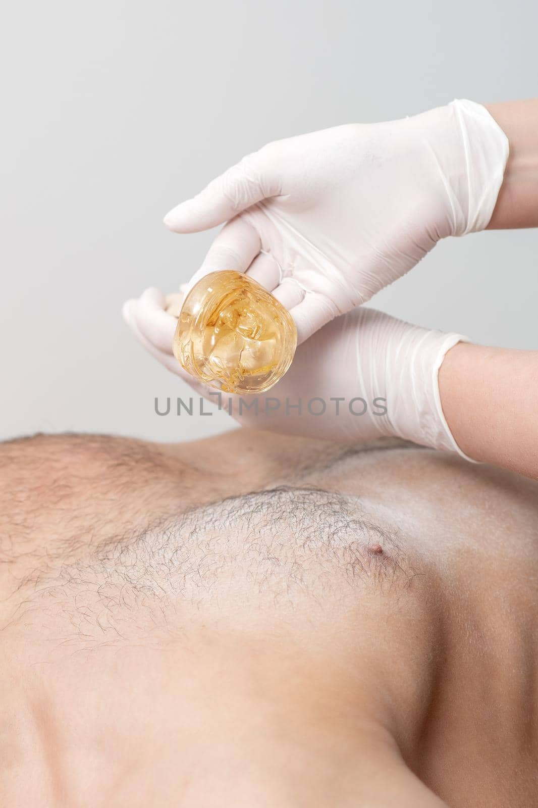 Epilation chest of young male with liquid wax paste by hands of female cosmetologist in beauty salon