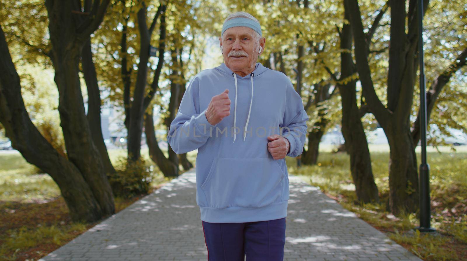 Athletic fitness senior elderly sport runner man training, listening music in earphones. Workout cardio outside in park at morning. Grandfather enjoying healthy lifestyle. Active retired mature people