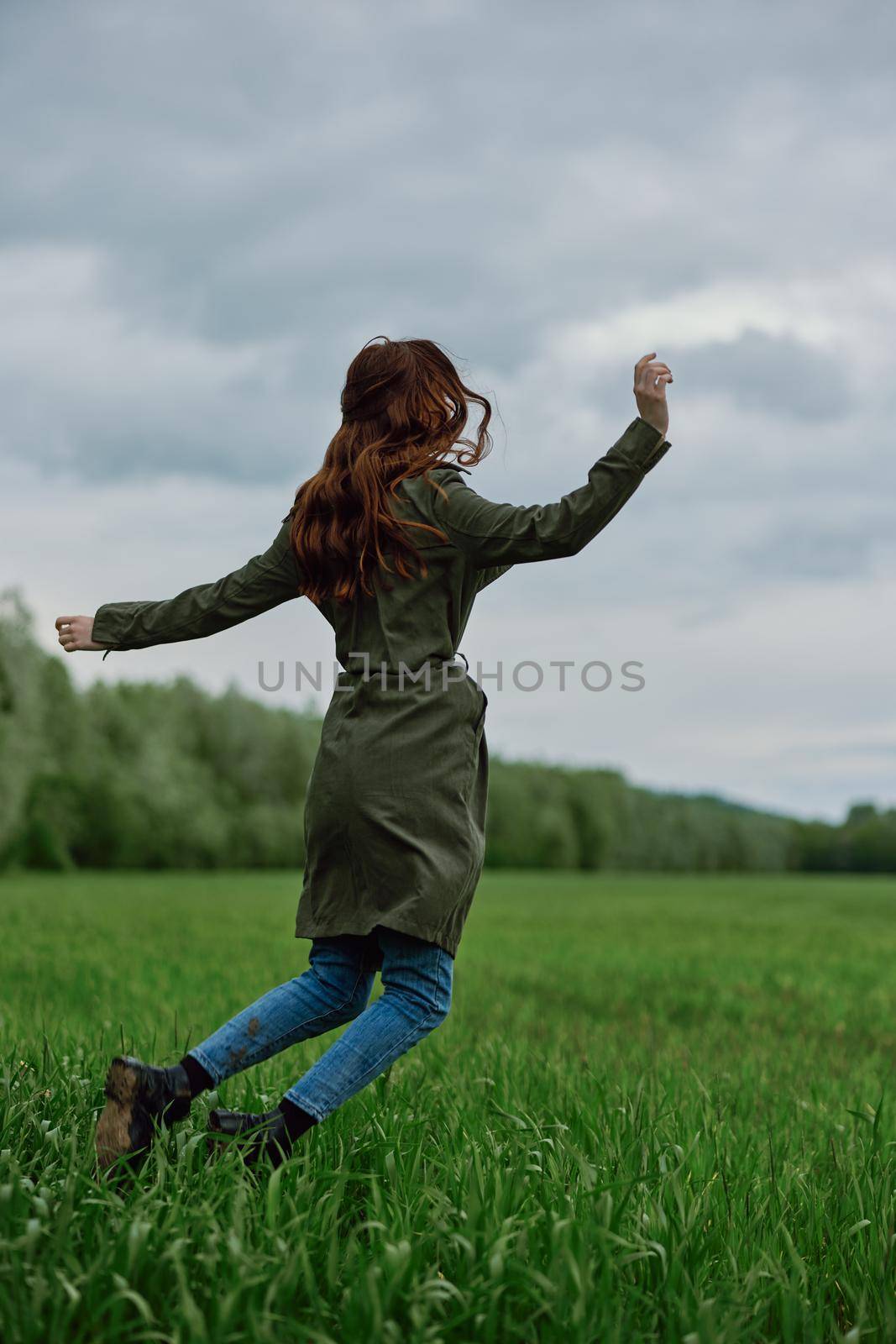 happy woman in a long raincoat jumping in a green field in cloudy weather. High quality photo
