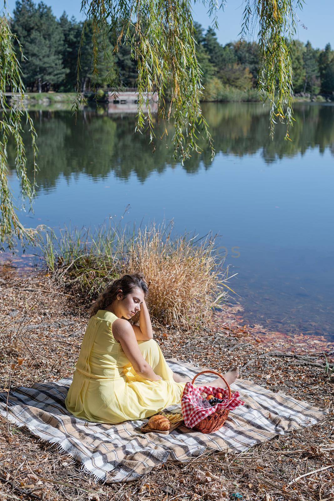 Leisure, free time. Beautiful caucasian woman in yellow dress on a picnic outdoors, sitting next to water