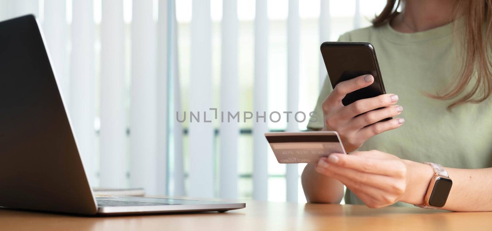 Close up female hands holding credit card and smartphone, young woman paying online, using banking service, entering information, shopping, ordering in internet store, doing secure payment by wichayada