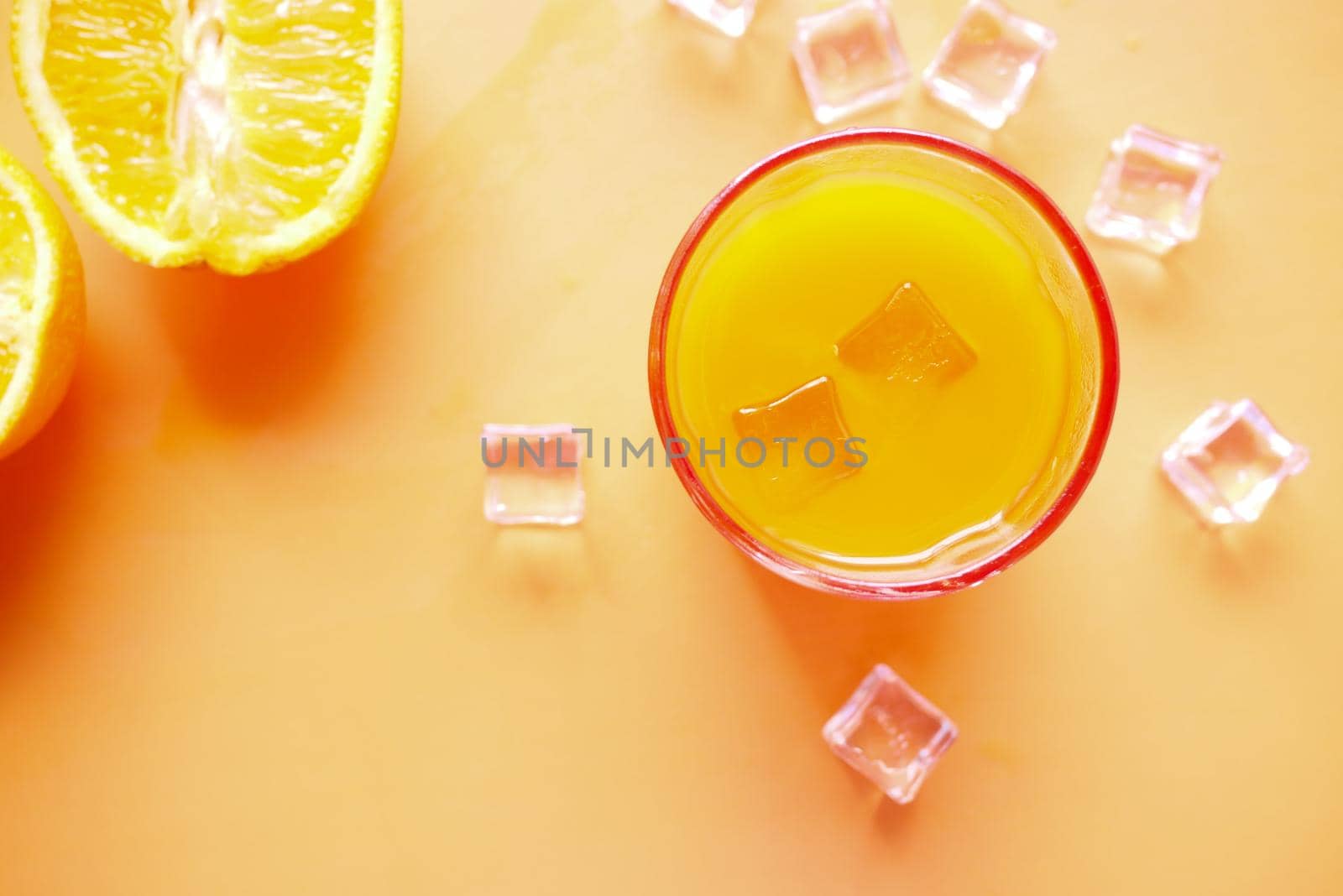orange juice and ice cube in glass on a color background .