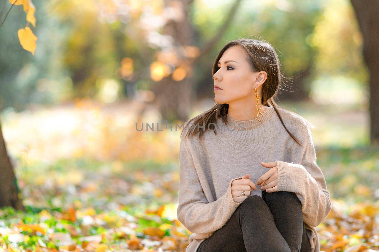 Young pensive mixed race woman sitting on the grass in the park in early autumn.