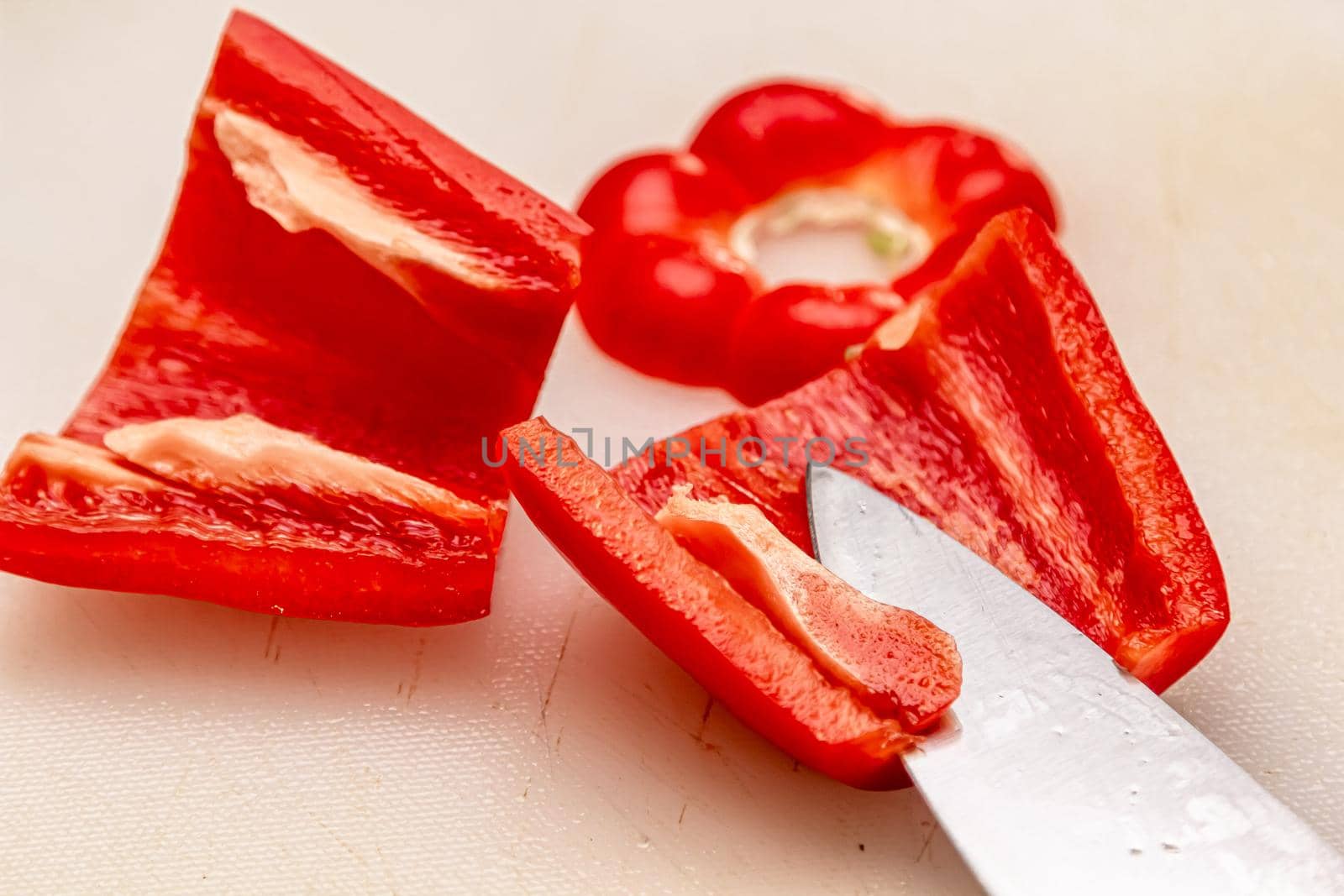 Close up view of a red bell pepper cut in half. The seeds are in the pepper on a cutting board. A knife is in the background.