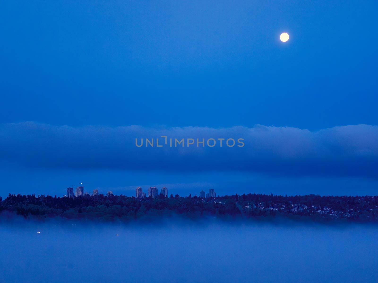 Night city in clouds with full moon over in the sky.