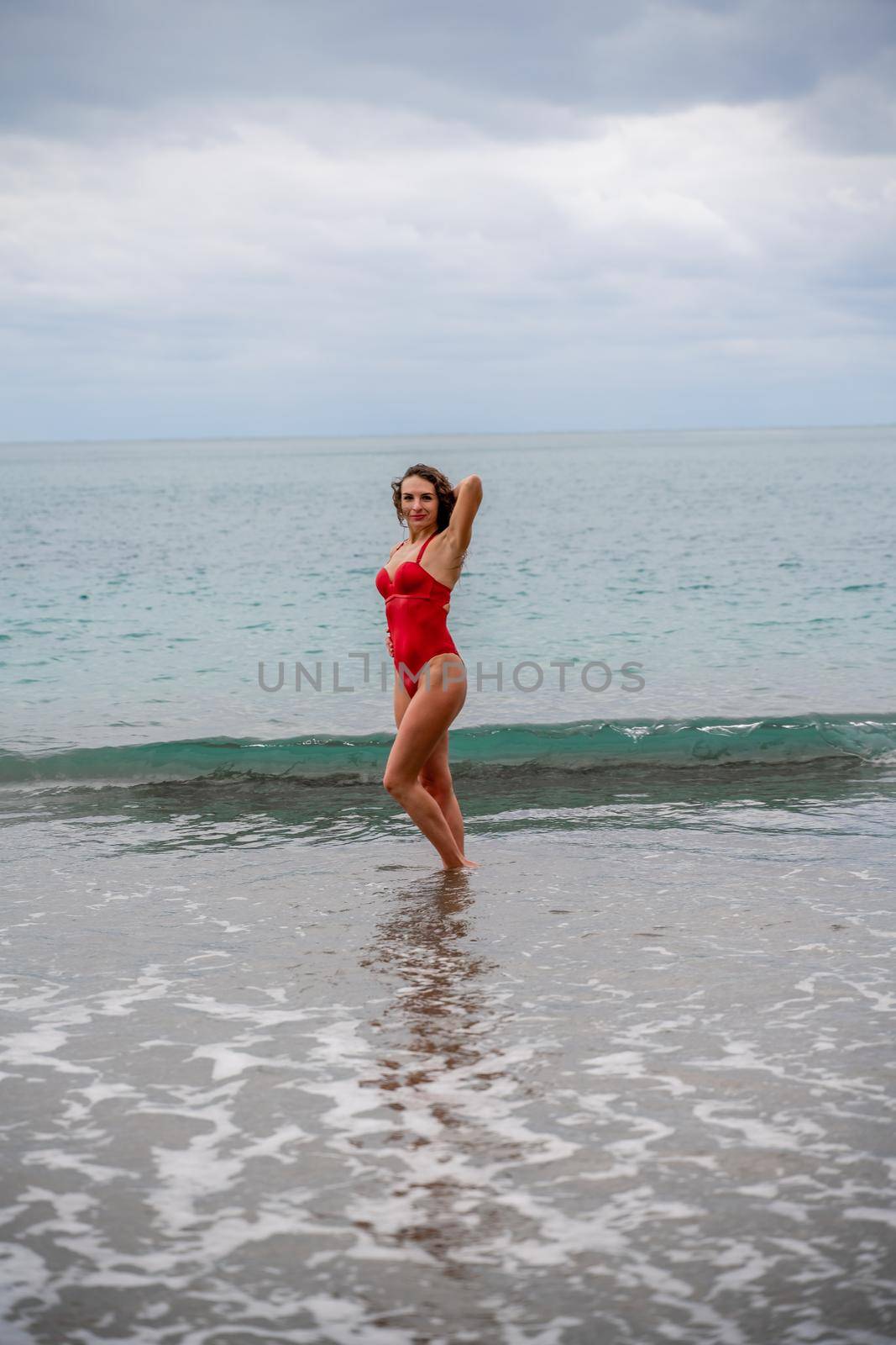 A beautiful and sexy brunette in a red swimsuit on a pebble beach, Running along the shore in the foam of the waves by Matiunina