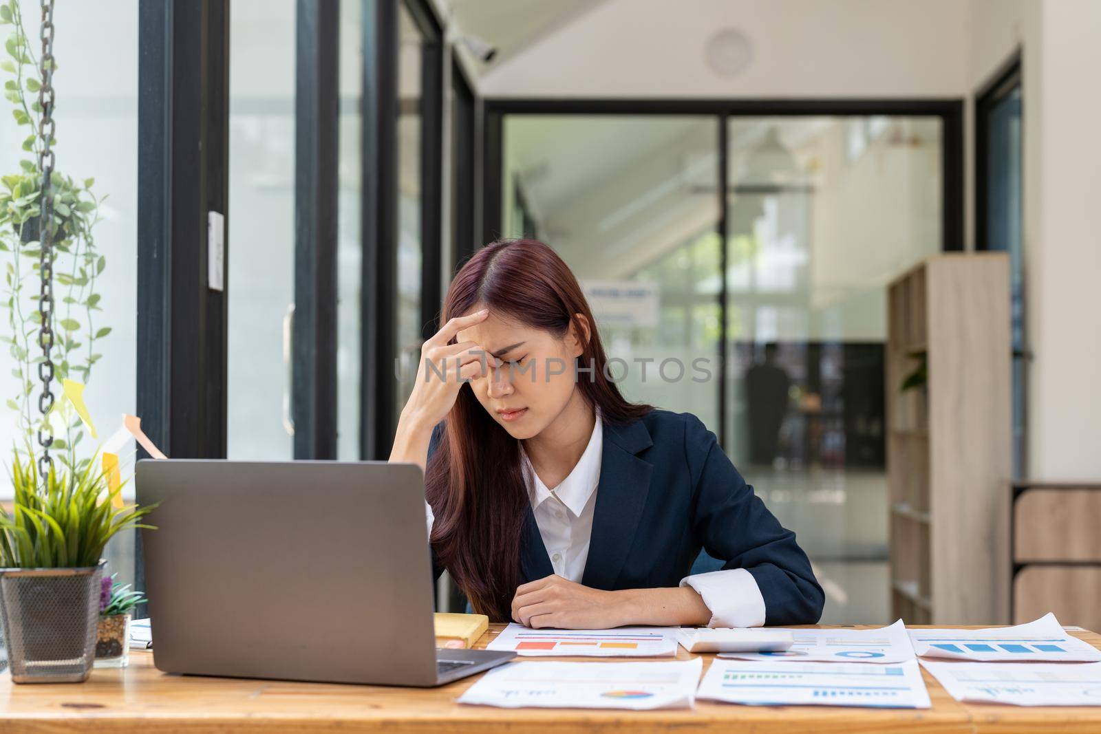 Tired business asian woman holds her fingers on her temples at work table. Irregular working day stressed worried, tired and overwhelmed concept.