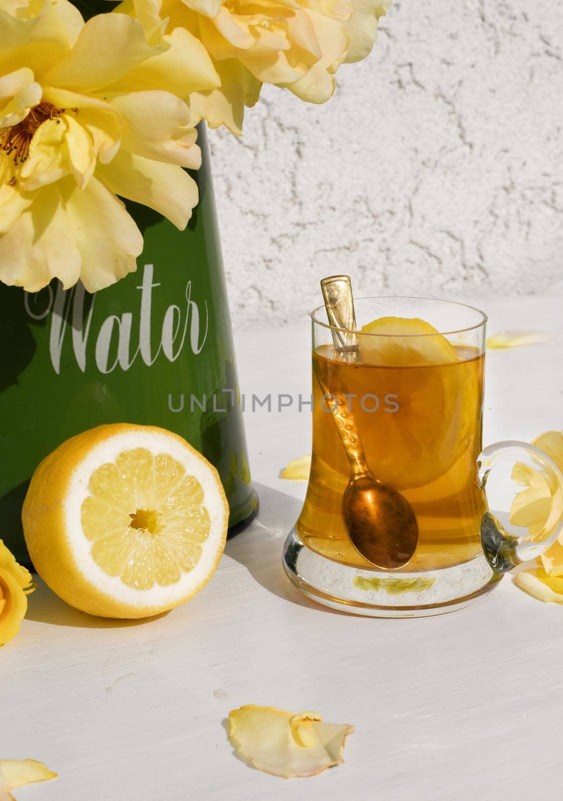 Yellow tea with lemon and a bouquet of yellow roses in a green jug, vintage still life . High quality photo