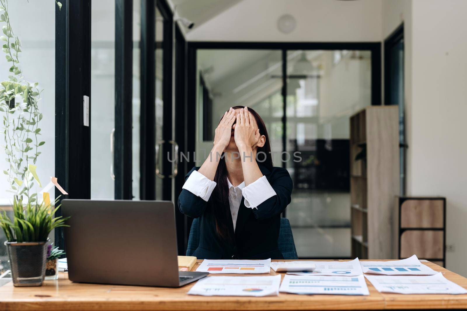 Tired business asian woman holds her fingers on her temples at work table. Irregular working day stressed worried, tired and overwhelmed concept.