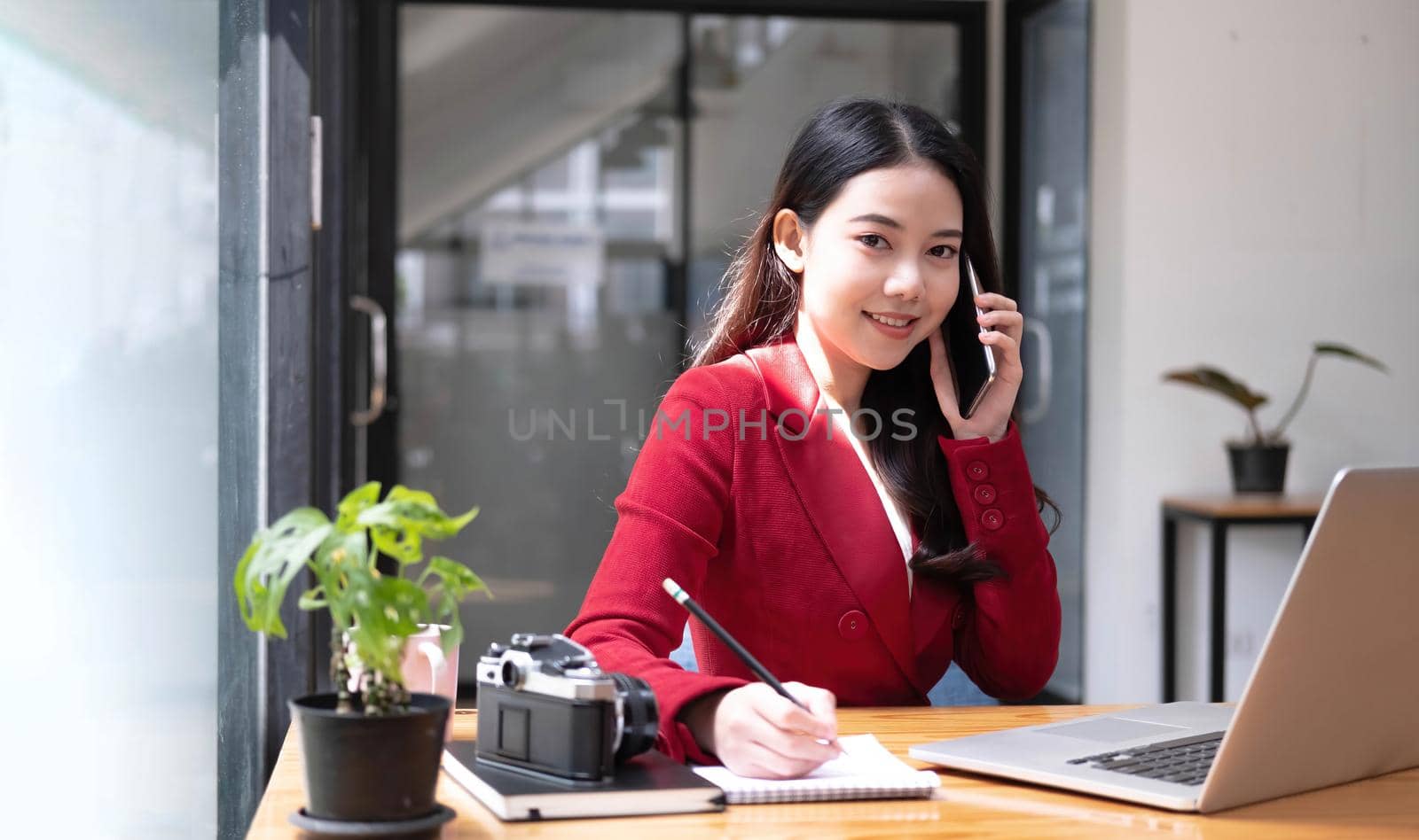 Charming Asian woman with a smile standing holding papers and mobile phone at the office..