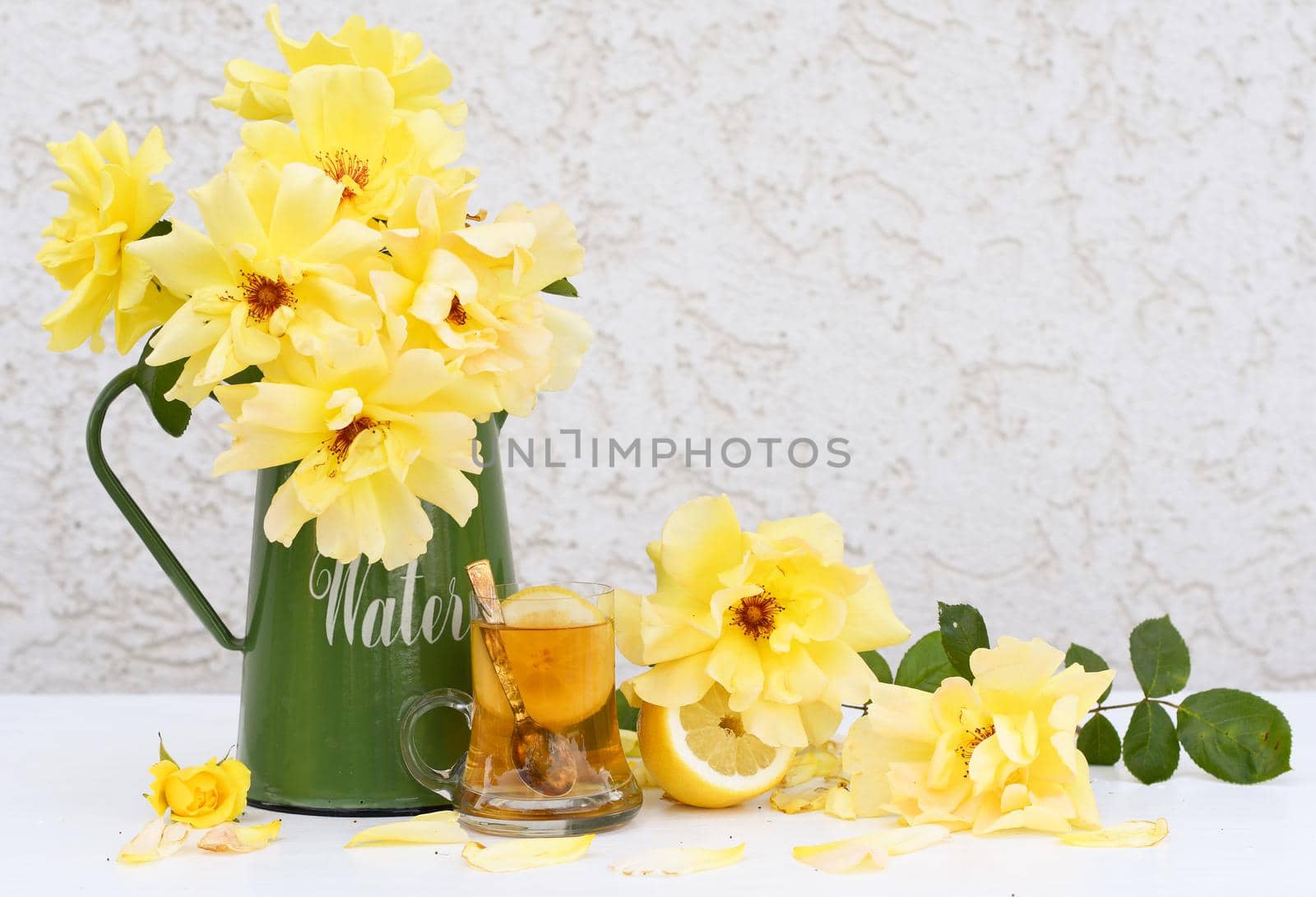 Yellow tea with lemon and a bouquet of yellow roses in a green jug, vintage still life . High quality photo
