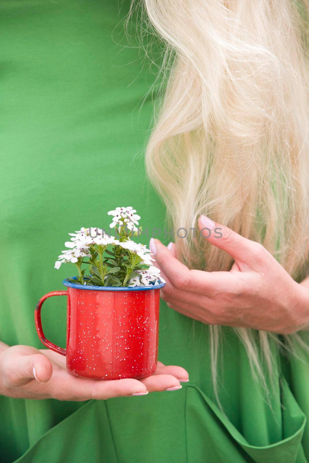 a blonde girl with long hair in a bright green dress holding a red mug with a bouquet of white flowers, portrait, High quality photo