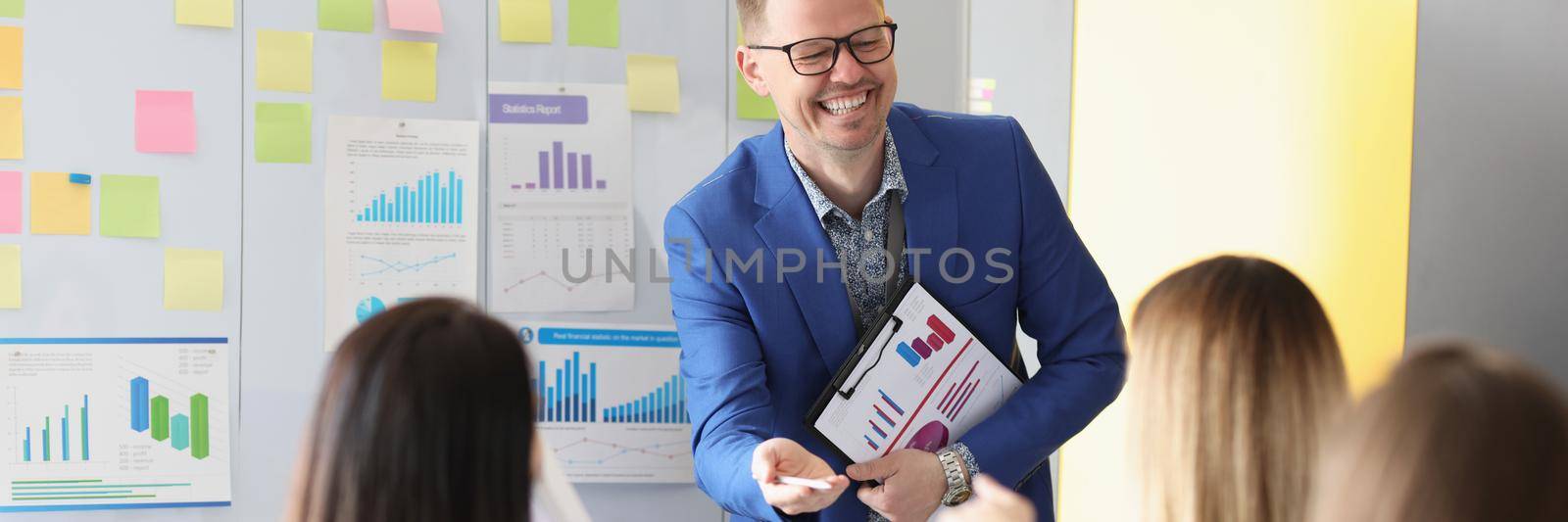 Portrait of laughing man speech giver stand in from of colleagues and explain something. Training for company workers, skills development. Business concept