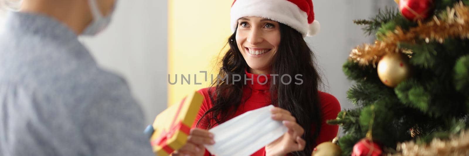 Portrait of smiling woman opened present box and got face mask as gift. Protection from virus spread, decorated christmas tree. New year, infection concept