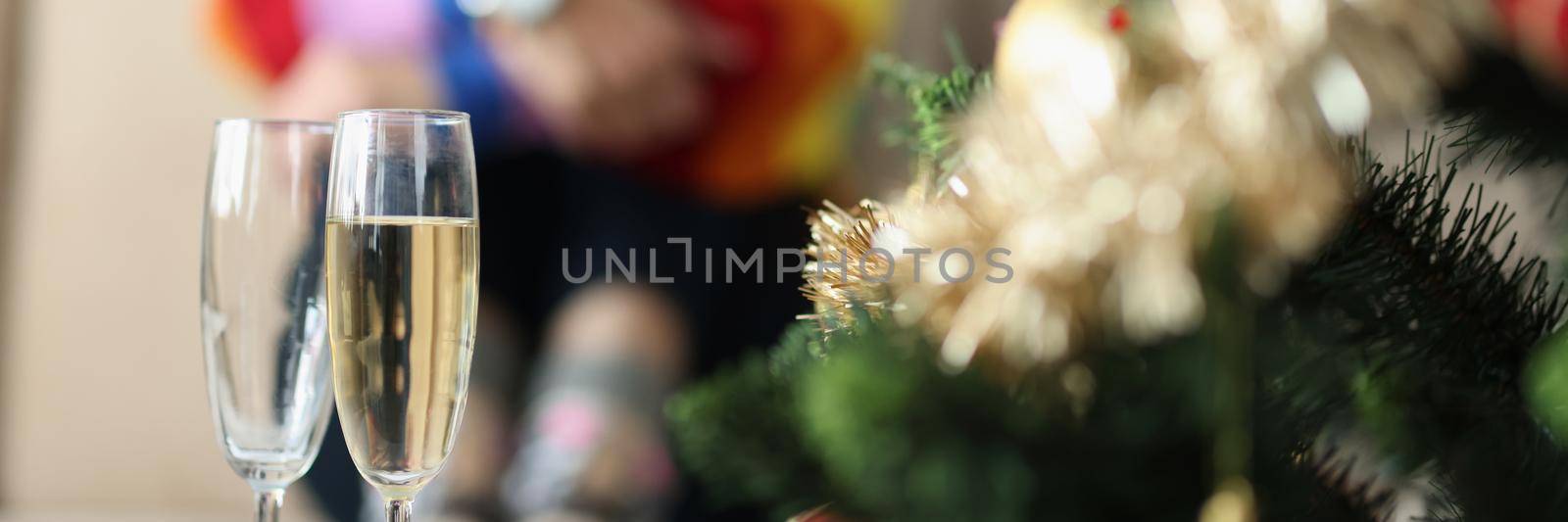 Close-up of two glasses near decorated christmas tree and sad woman sitting alone. Broke up with girlfriend on new year. Christmas holiday, lgbt concept