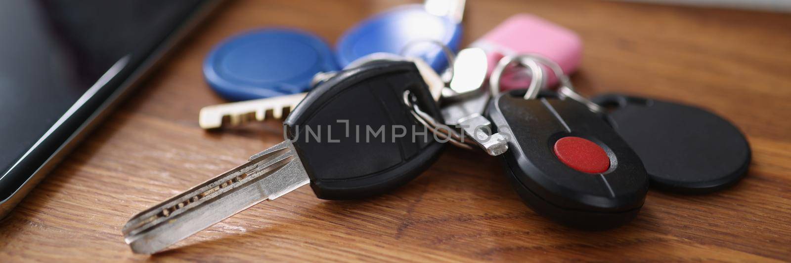 Close-up of bundle of car remote keys and keys from home and buzzer. Smartphone with black screen on wooden table. Access to your property, mockup concept