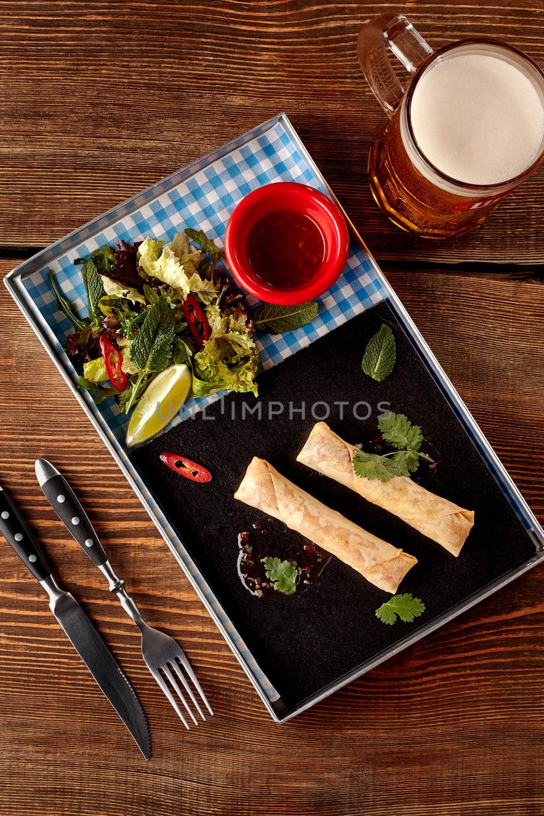 Spring rolls with sweet chili sauce, salad and beer on wooden table. Top view. Still life. Photo for the menu