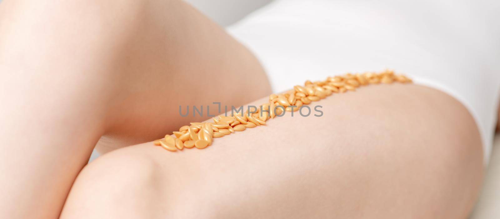 Wax beans or seed in row on legs of young woman lying on white background