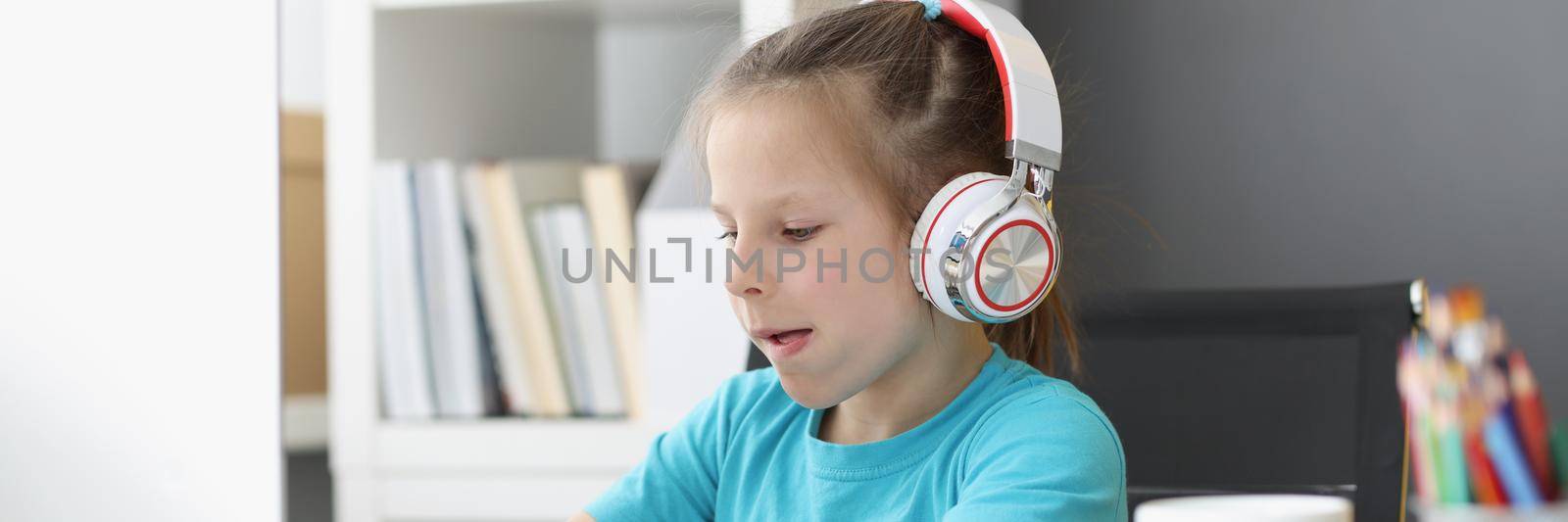 Portrait of cute kid wearing headset and typing on keyboard with effort. Child explore new technology, try computer in use. Childhood, development concept