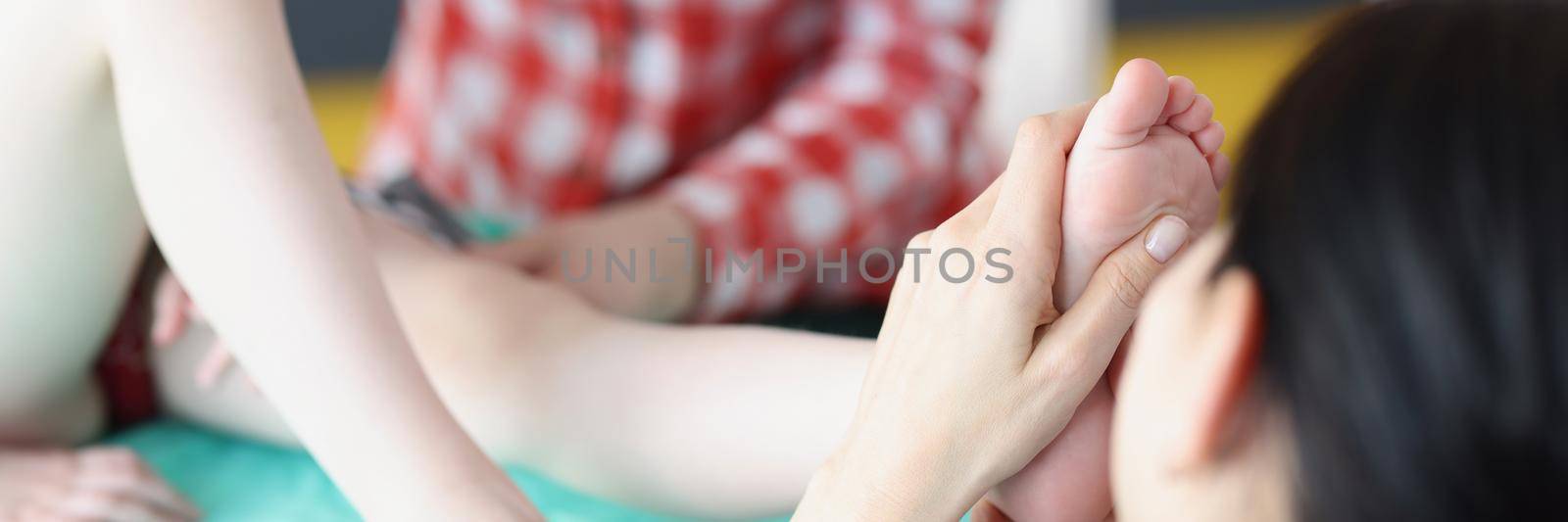 Close-up of woman physiotherapist massaging childs feet on appointment in clinic. Leg damage after injury or accident. Healthcare, medicine, care concept