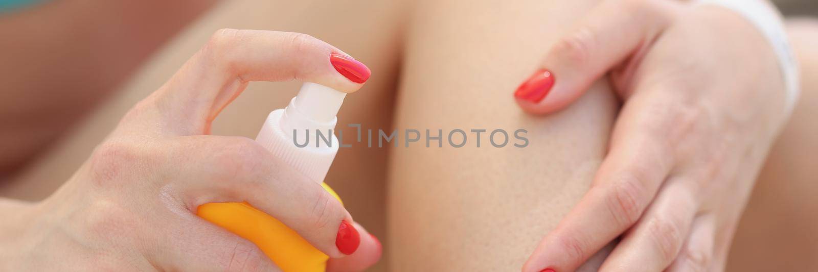 Close-up of woman applying protective sunscreen lotion on leg. Female hand with perfect manicure holding cosmetic product from sun. Skincare and sunburn concept