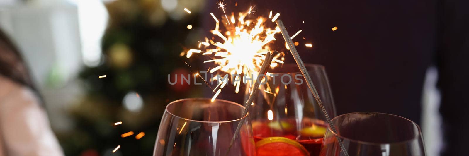 Close-up of people holding fire sparklers and glass filled with champagne and celebrate new year. Party, nightlife and new year holiday. Christmas concept
