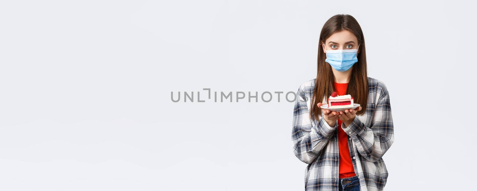 Coronavirus outbreak, lifestyle during social distancing and holidays celebration concept. Young cute girl in medical mask and casual outfit, holding birthday cake and looking serious camera by Benzoix