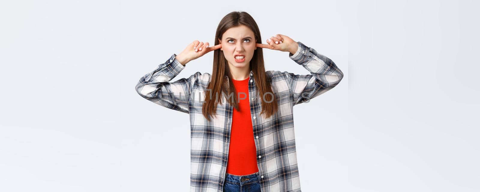 Lifestyle, different emotions, leisure activities concept. Pissed-off angry young female student in dormitory bothered by loud neighbours upstairs, staring up furious, shut ears from noisy music.