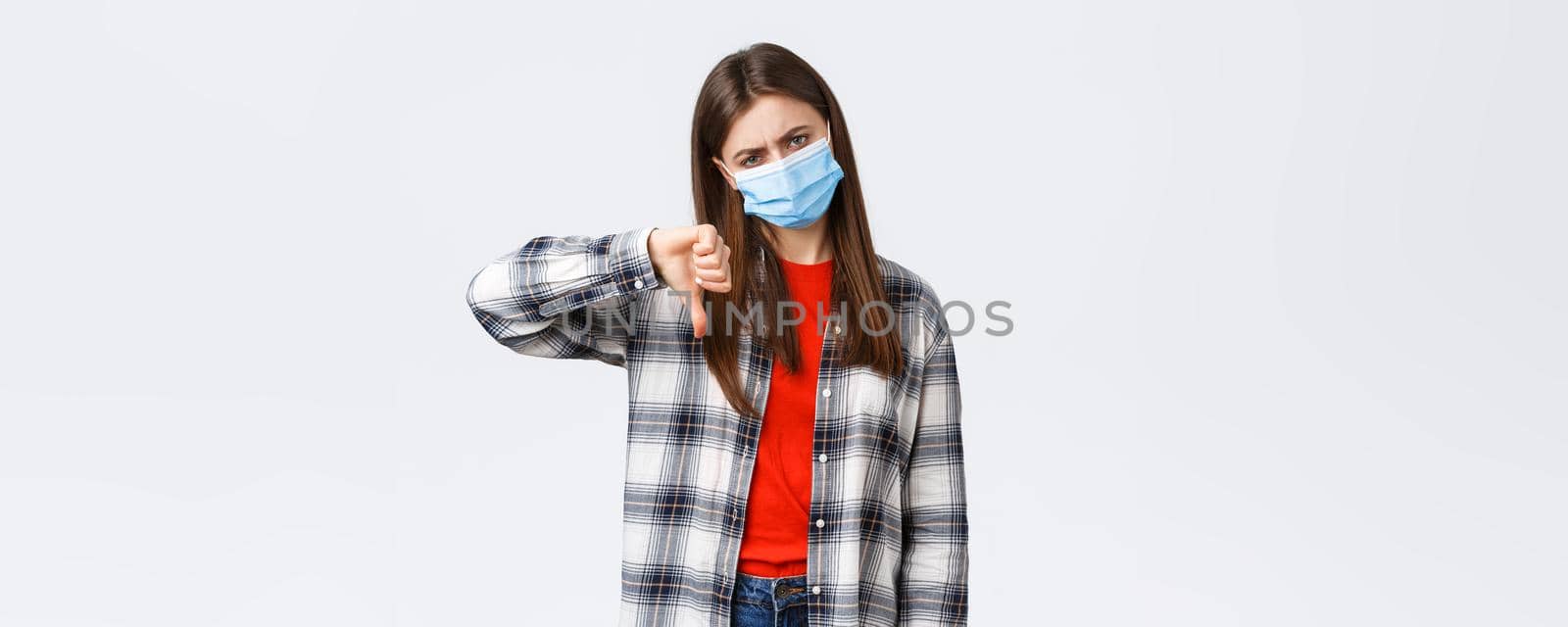 Coronavirus outbreak, leisure on quarantine, social distancing and emotions concept. Lame bad idea. Displeased and unamused young woman in medical mask thumb-down in disapproval.