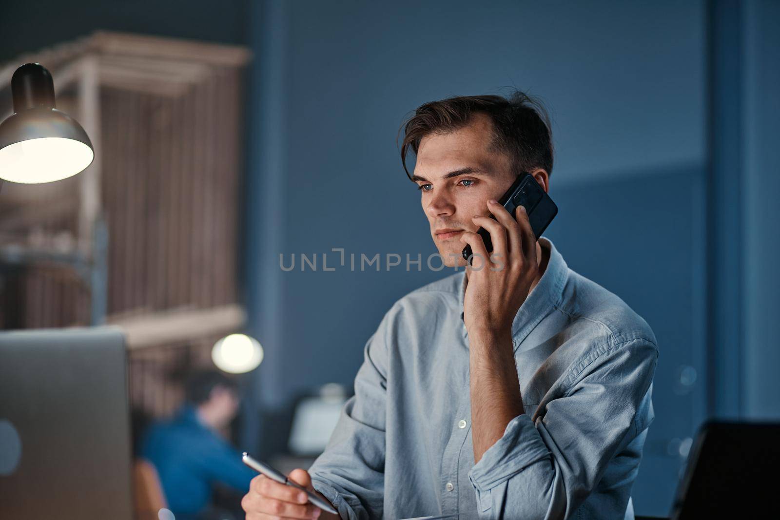 young businessman making a call from the office at night. by SmartPhotoLab