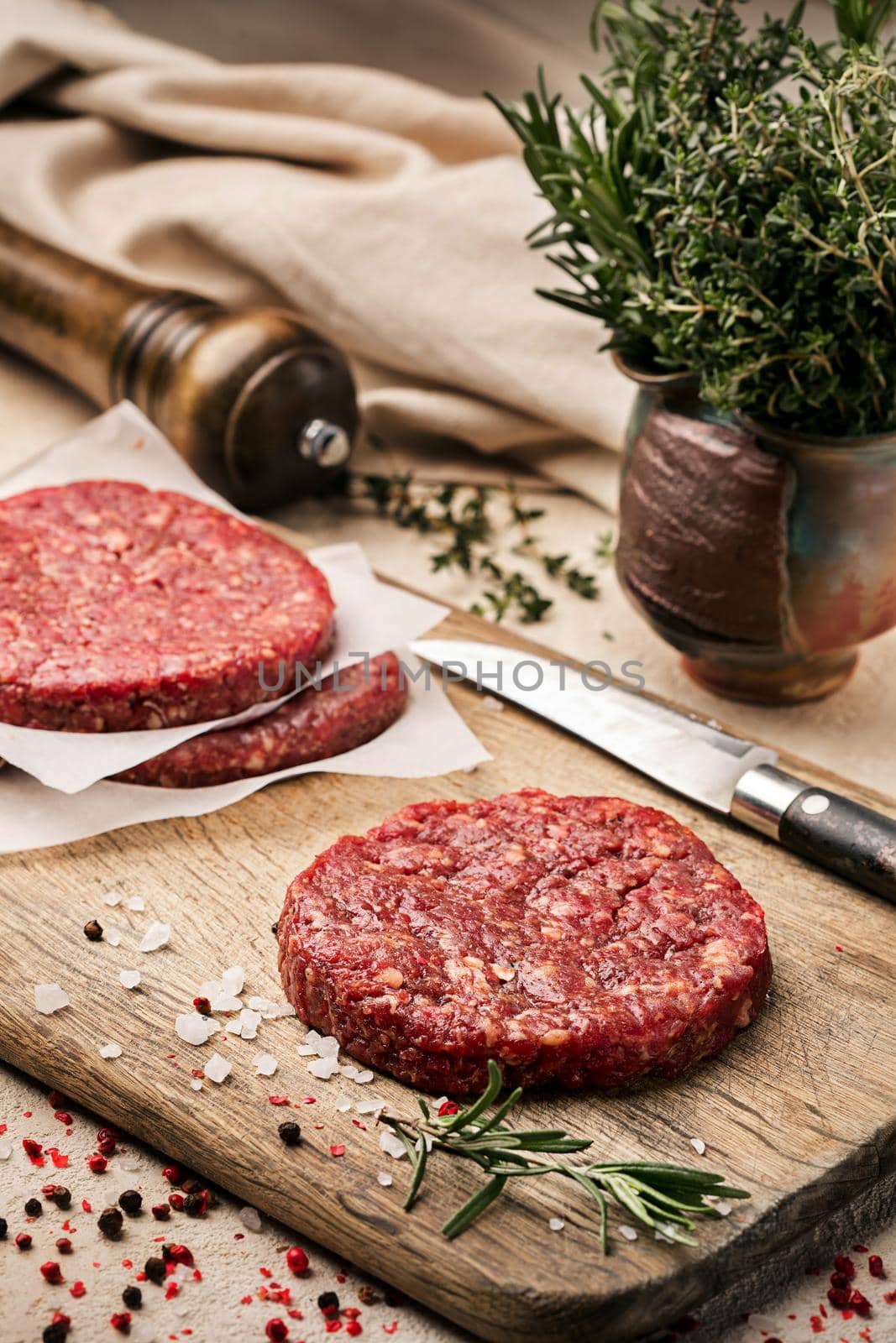 On a wooden cutting board on kraft paper there are raw beef burgers for burgers, spices, rosemary, a pepper mill, a cooking process. Top view. Still life. Copy space. Flat lay