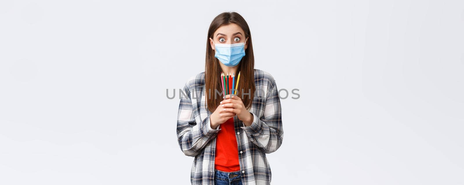 Social distancing, leisure and hobbies on covid-19 outbreak, coronavirus concept. Enthusiastic cute girl in medical mask trying new thing on self-quarantine, showing colored pencils, learn how draw by Benzoix