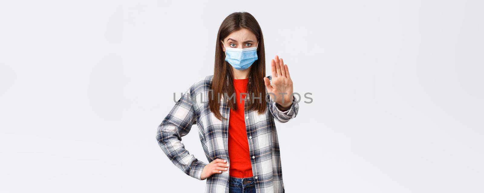 Coronavirus outbreak, leisure on quarantine, social distancing and emotions concept. Where you think going. Displeased young woman in medical mask, stretch hand forward in stop gesture.