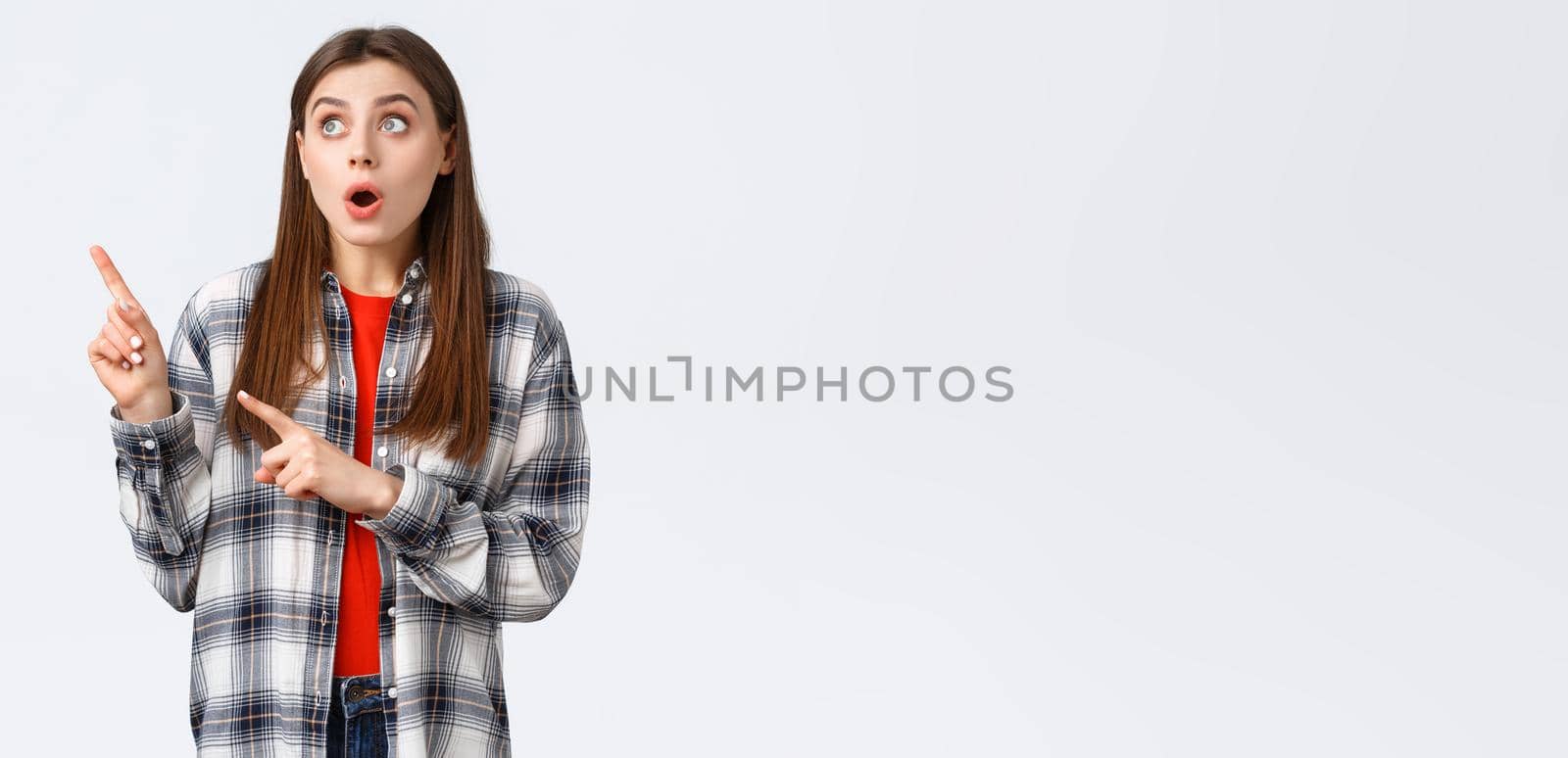 Lifestyle, different emotions, leisure activities concept. Amused attractive girl, european woman in checked shirt pointing and looking upper left corner, captured attention to awesome promo.
