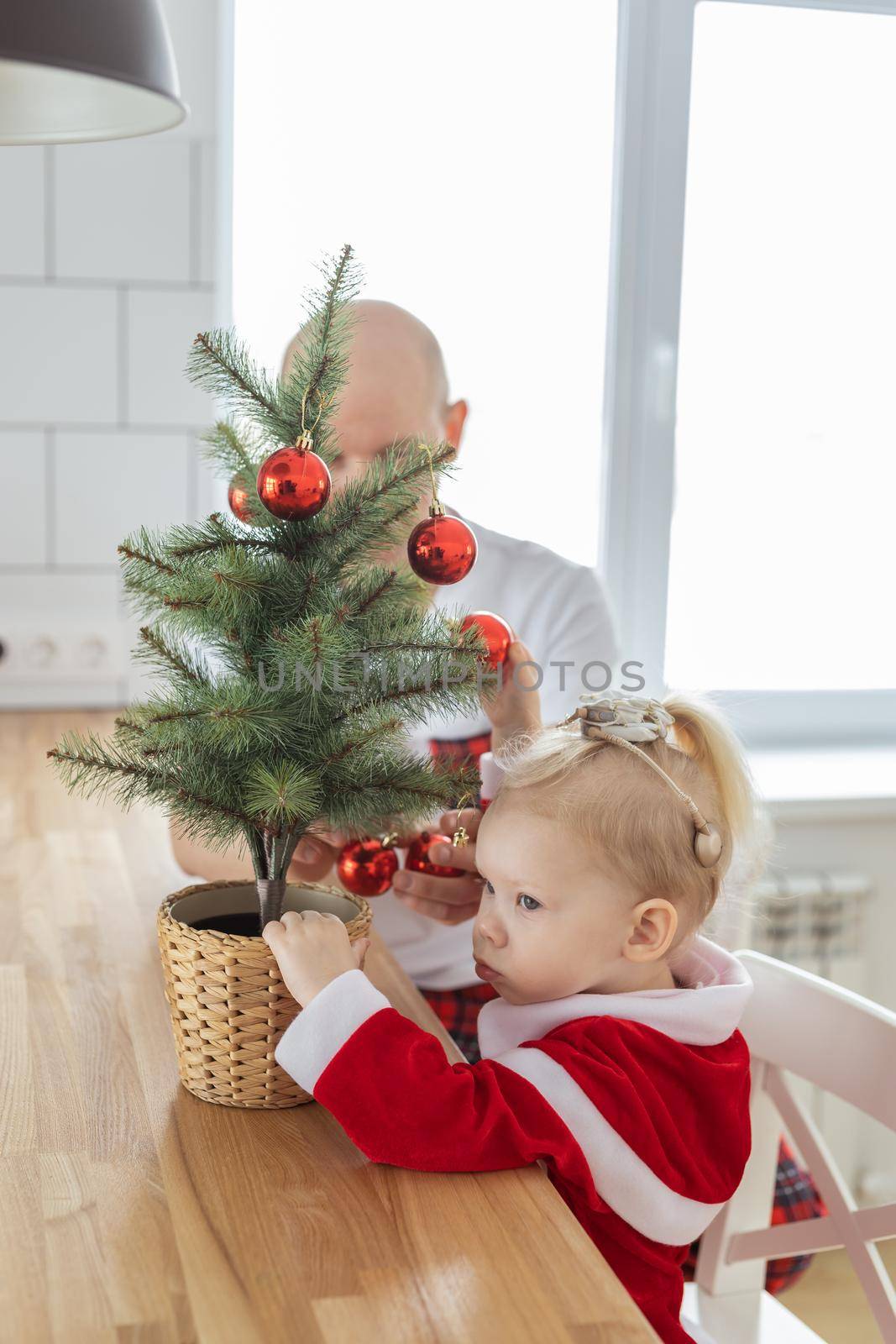 Child with cochlear implant hearing aid having fun with father and small christmas tree - diversity and inclusion and deafness treatment and medical innovative technologies by Satura86