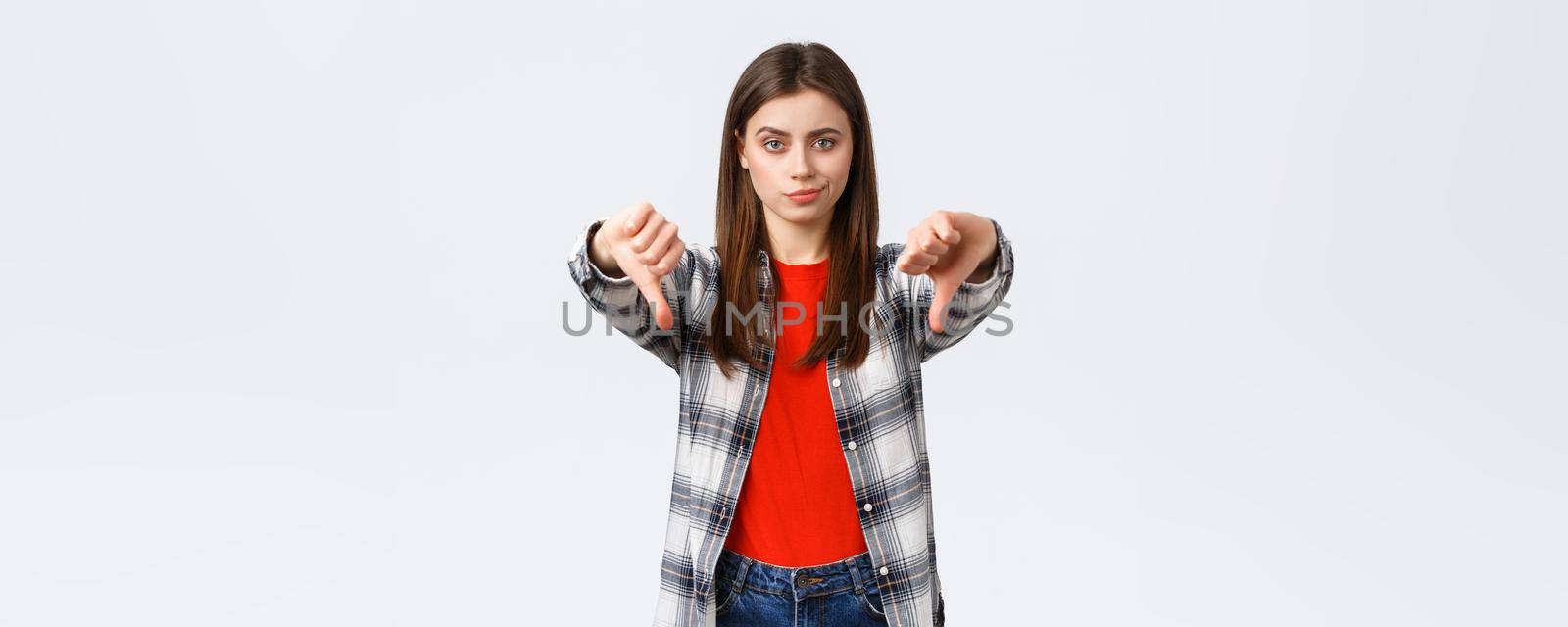 Lifestyle, different emotions, leisure activities concept. Skeptical and disappointed young woman smirk unsatisfied and showing thumbs-down in dislike, disapprova and judging bad product.