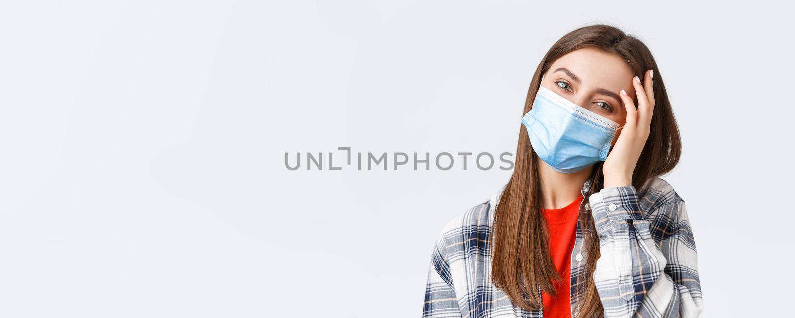 Coronavirus outbreak, leisure on quarantine, social distancing and emotions concept. Close-up of tender happy young woman in medical mask, tilt head, flirting and playing with hair by Benzoix