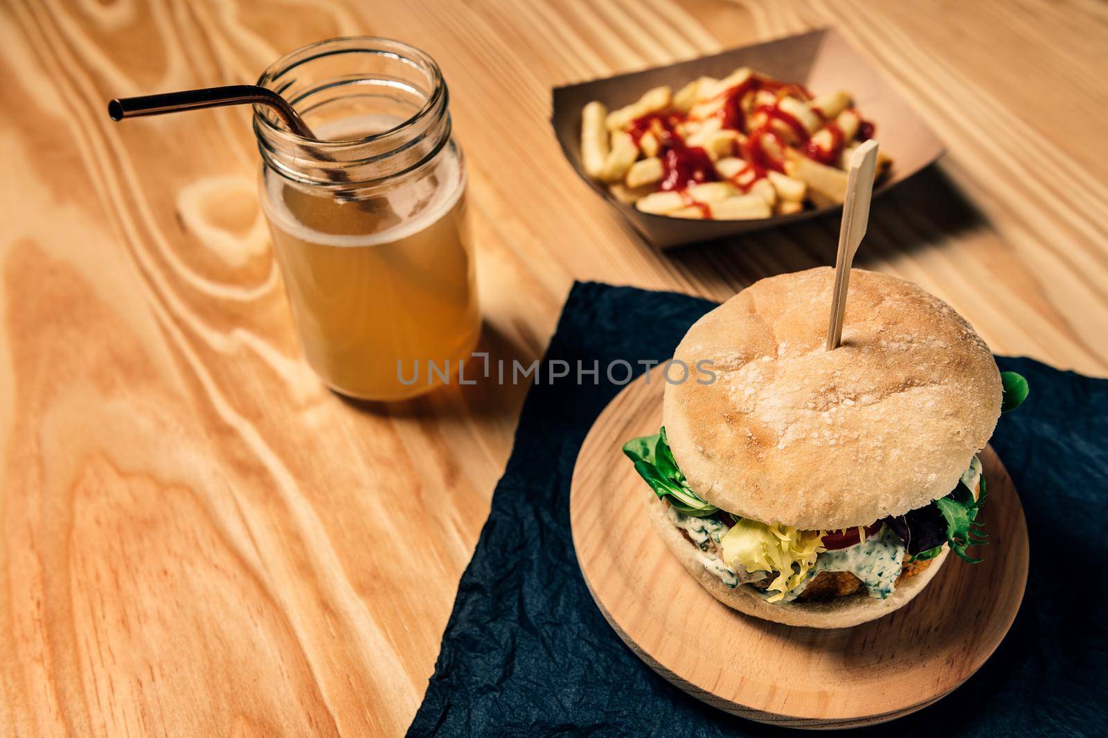 gourmet vegan burger with lettuce and sauce on a wooden table with french fries with ketchup in a cardboard tray and a healthy drink, veggie food and foodie lifestyle concept, selective focus