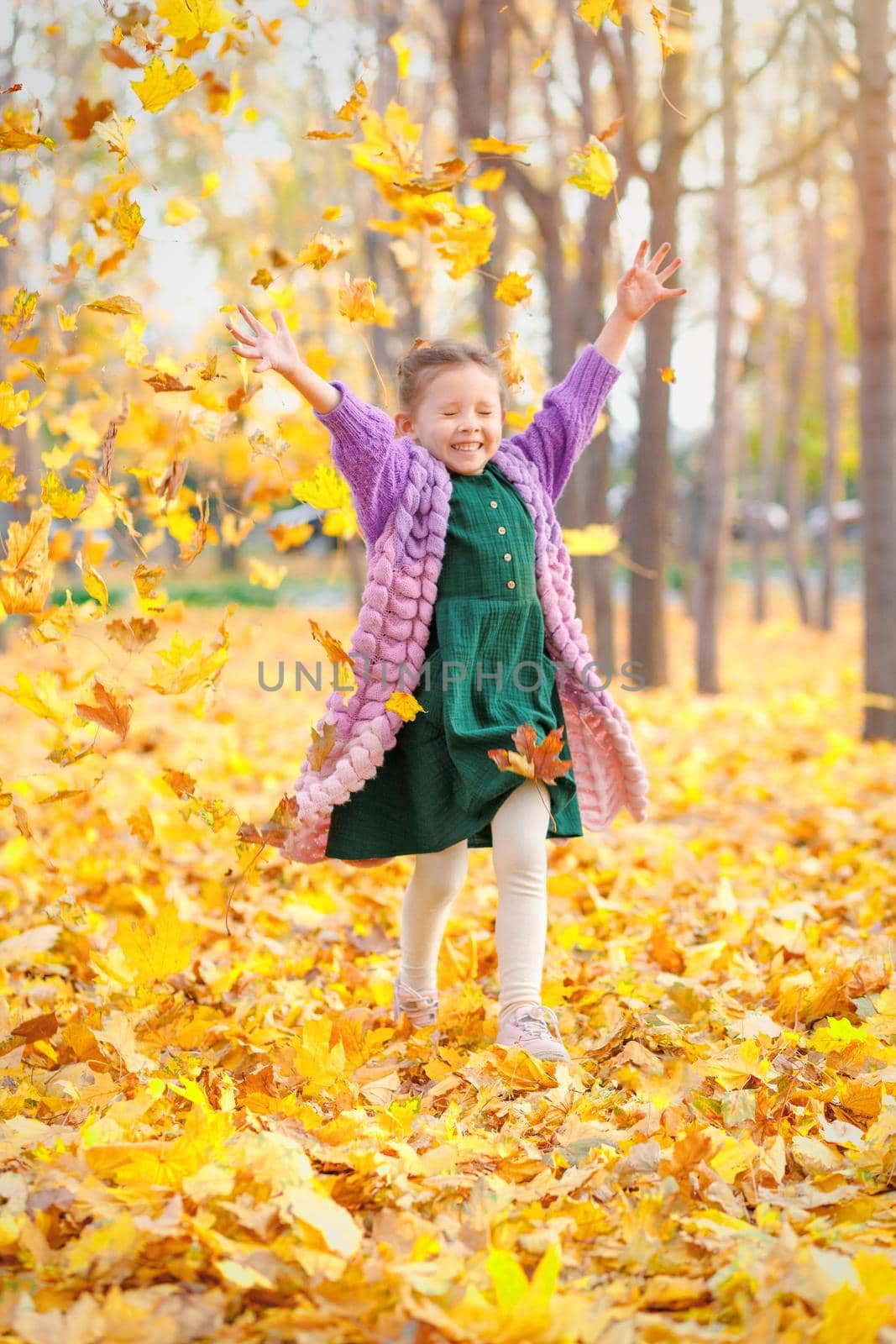 Smiling caucasian girl having fun in autumn park throws up fallen leaves.