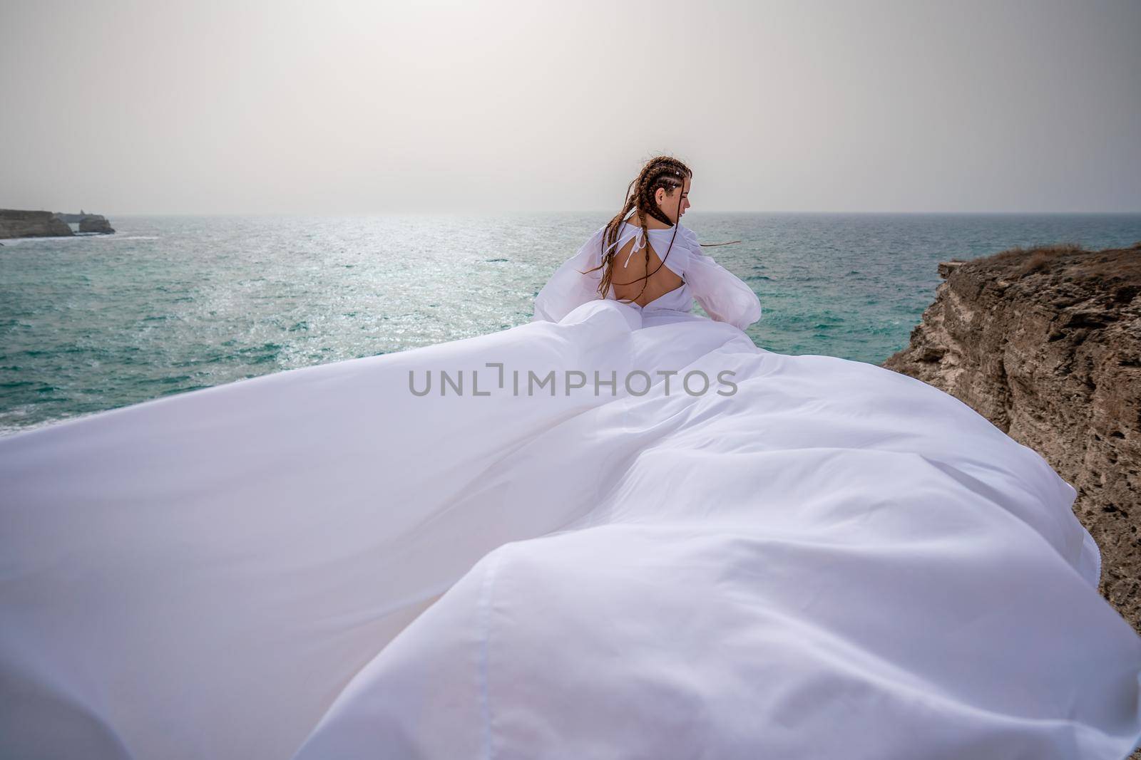 Happy freedom woman on the beach enjoying and posing in white dress. Rear view of a girl in a fluttering white dress in the wind. Holidays, holidays at sea