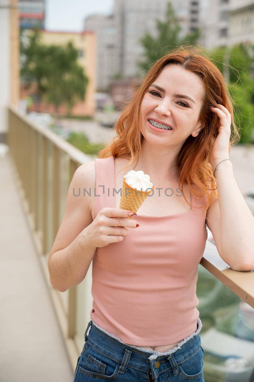 Portrait of young beautiful red-haired woman smiling with braces and going to eat ice cream cone outdoors in summer.